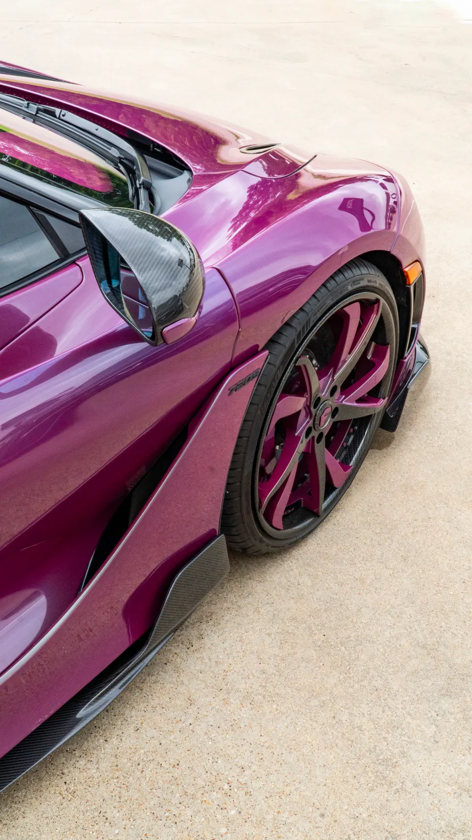 A close-up of a purple McLaren 720S featuring custom purple wheels, carbon fiber side skirts, and a carbon fiber mirror.