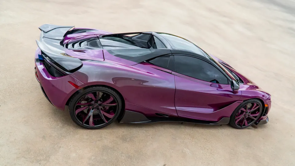 A vibrant purple McLaren 720S with custom wheels and a large rear wing, parked on a light-colored surface.
