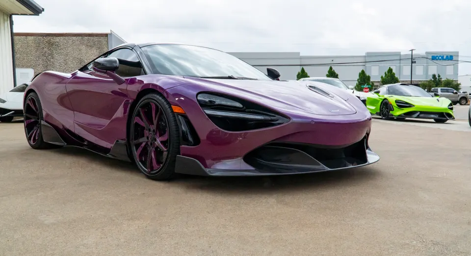 A custom purple McLaren 720S with aftermarket wheels and carbon fiber aero elements parked outdoors, with a green McLaren 720S in the background.