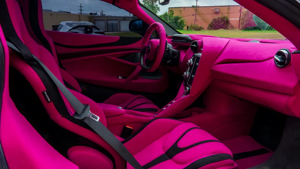 Detailed view of a McLaren's custom pink interior, featuring racing seats, harnesses, and a matching steering wheel.