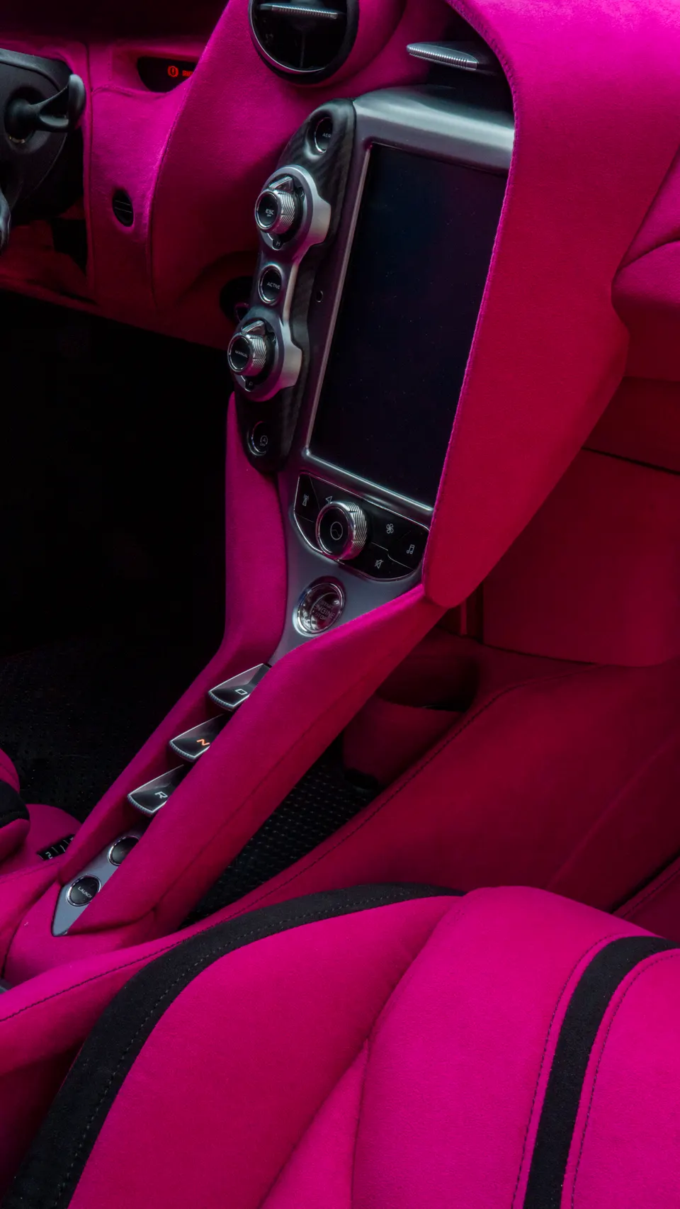 A close-up of a McLaren's custom pink Alcantara interior, showing the center console and infotainment screen.