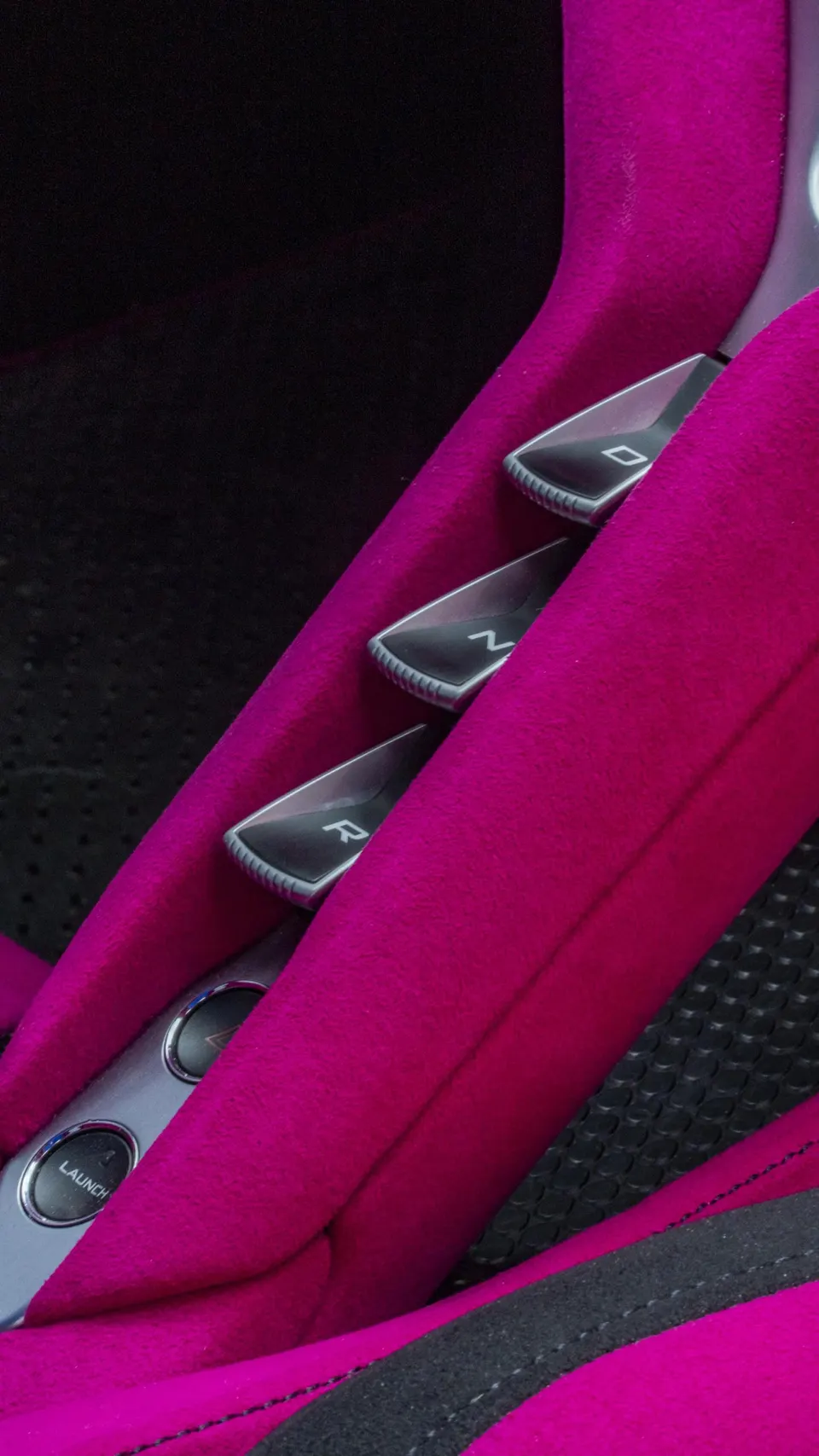 A close-up of a car's interior showing bright pink upholstery, gear selector buttons, and a launch control button.