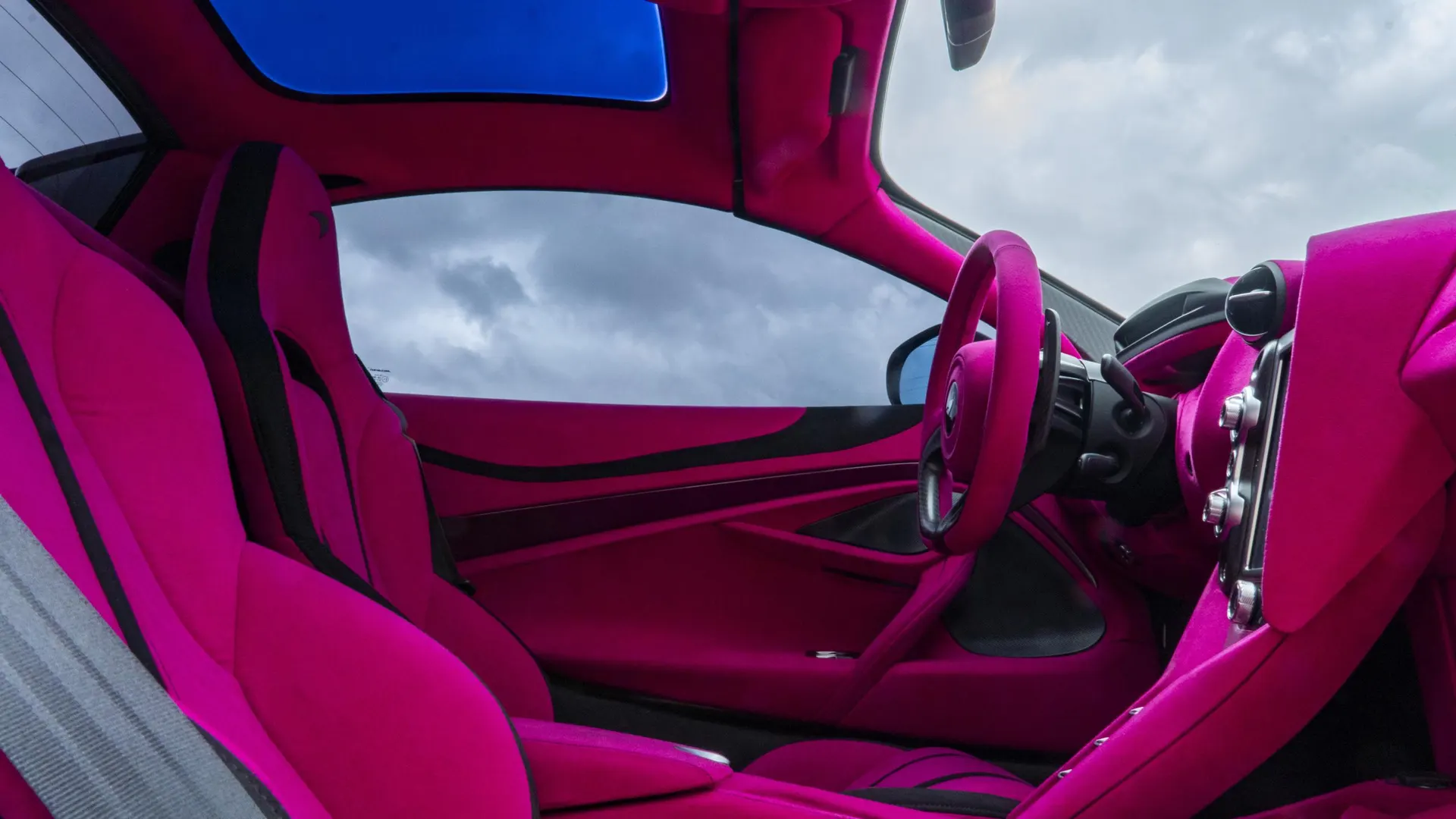 A detailed view of a McLaren's custom pink interior, featuring seats, steering wheel, and dashboard.