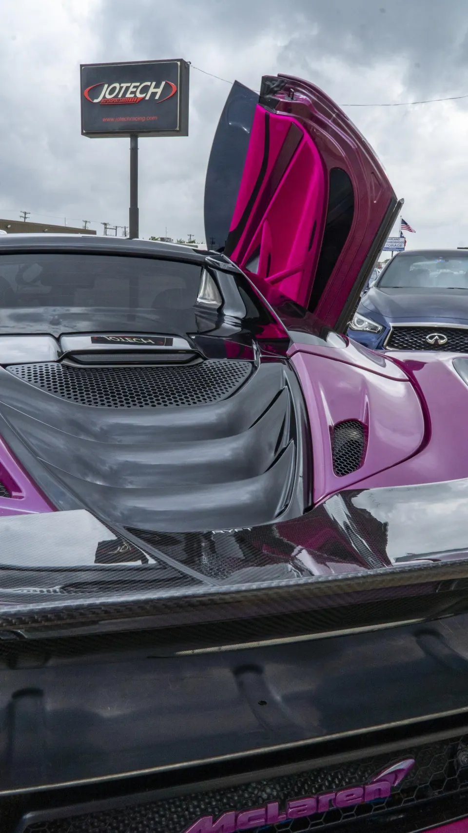 Purple and black McLaren with a custom wrap and carbon fiber body parts, parked outside Jotech Racing with its scissor door open.