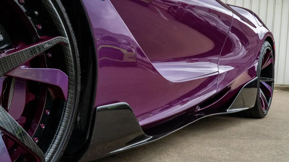 Close-up of a purple supercar's custom wheel and carbon fiber side skirt, showcasing exterior modifications.