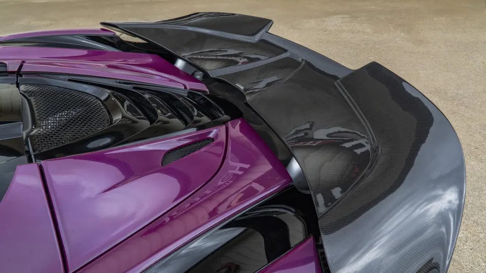 Close-up of a purple McLaren's rear, showcasing a large carbon fiber aerodynamic wing and engine cover.