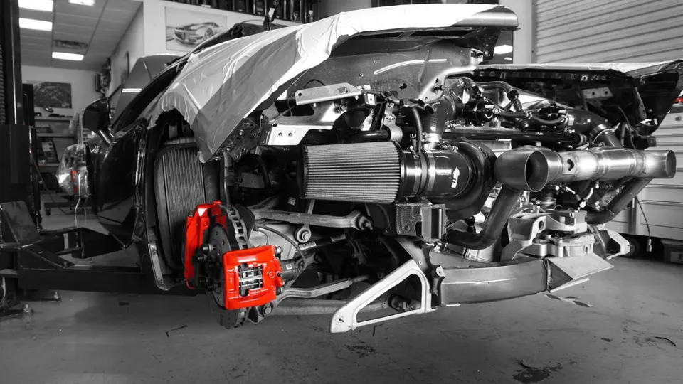 A disassembled C8 Corvette in a shop, showcasing a large turbocharger, custom exhaust, and red brake calipers.