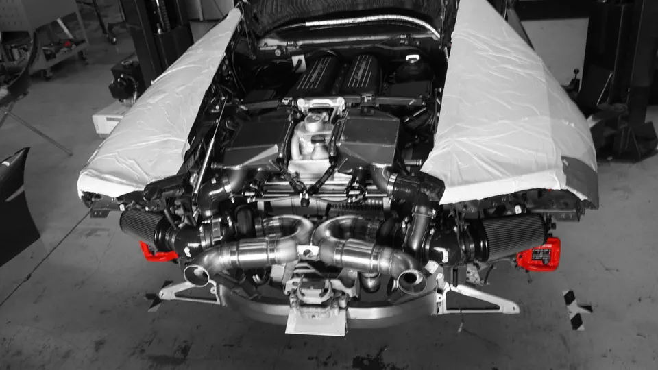 Lamborghini engine bay with custom twin-turbo setup and performance exhaust in a tuning shop.