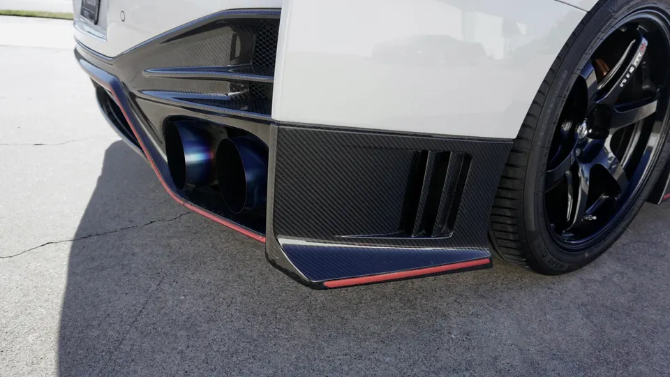 Close-up of a white Nissan GT-R's rear with a carbon fiber diffuser, titanium exhaust tips, and Nismo wheel.