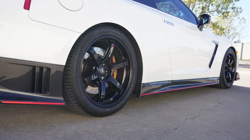 A white Nissan GT-R with black Nismo wheels, orange Brembo calipers, and carbon fiber side skirts parked outdoors.