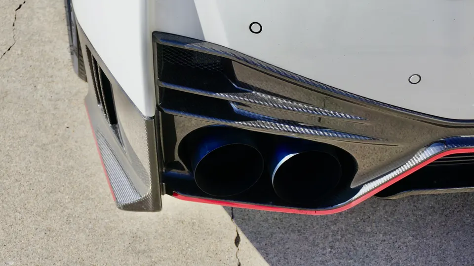 Close-up of a white car's rear bumper featuring blue-tinted titanium exhaust tips and a carbon fiber diffuser.