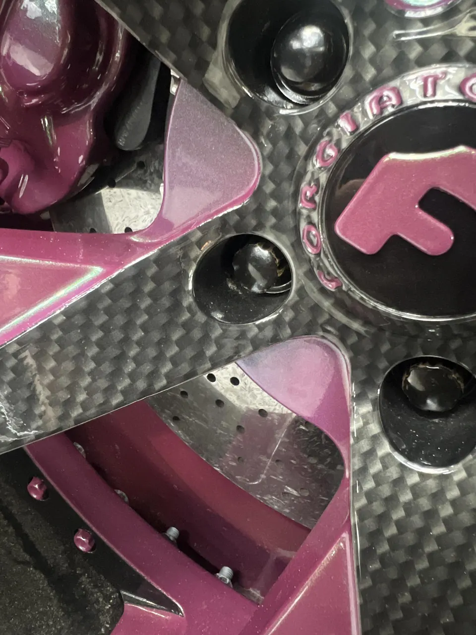 Close-up detail of a purple brake caliper behind a carbon fiber forged wheel with a custom center cap.