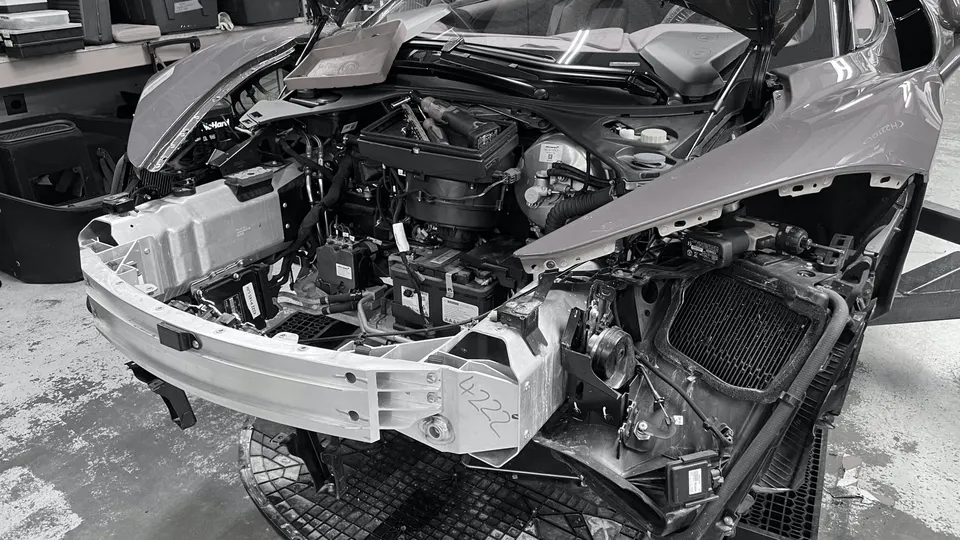A McLaren supercar undergoing front-end disassembly in a workshop, revealing internal components and crash structure.