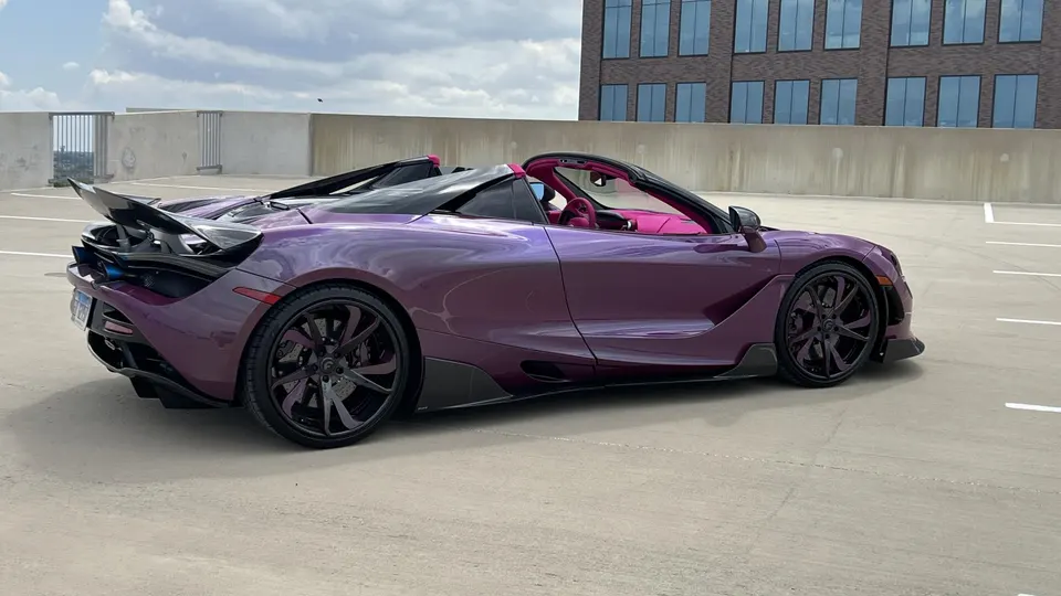 A stunning purple McLaren 720S convertible parked on a rooftop parking garage with a city skyline in the background.