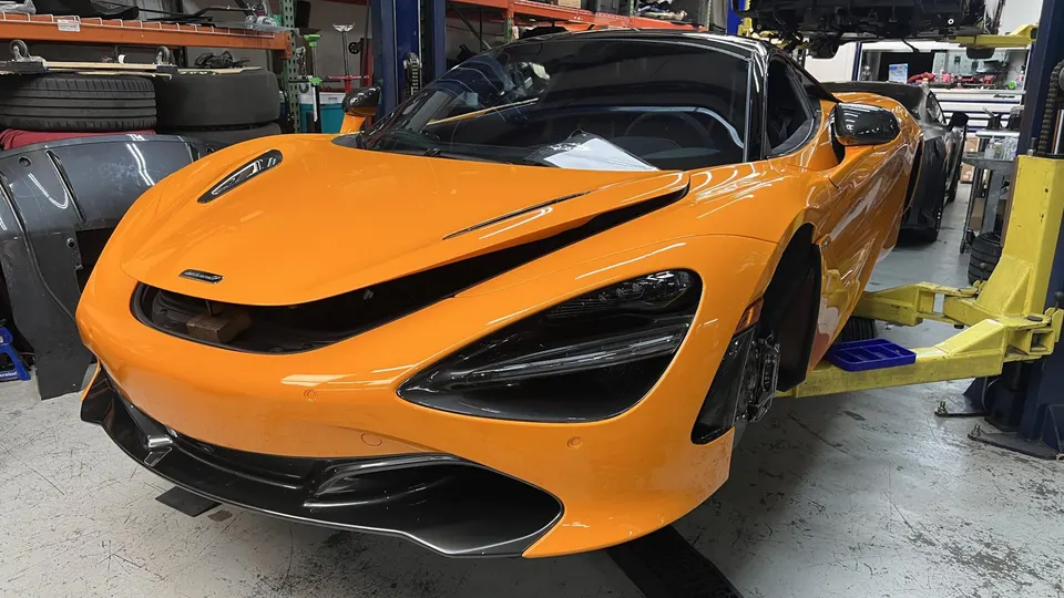 An orange McLaren 720S supercar on a lift in a performance tuning shop, undergoing maintenance or modification.