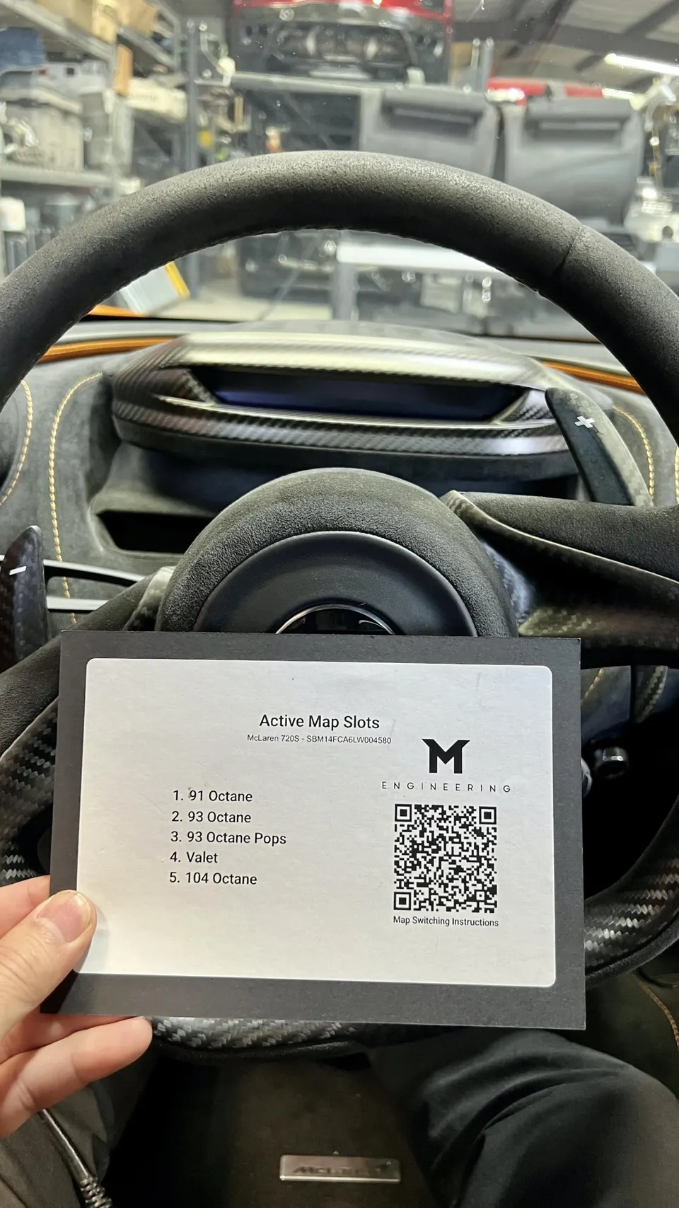 Close-up of a McLaren 720S interior showing the steering wheel and a card detailing active engine tuning maps for various octane levels.