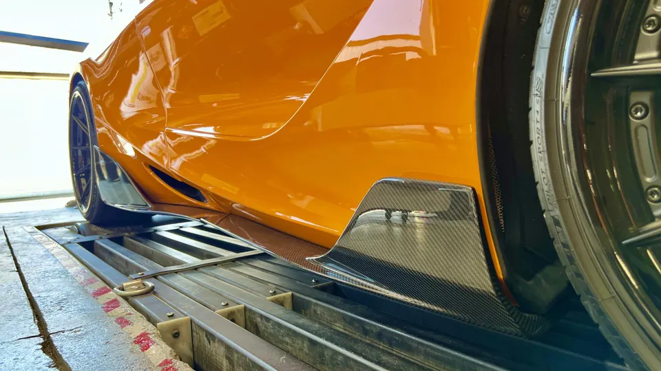 Orange McLaren supercar on a dyno, showcasing carbon fiber side skirts and rear wheel.