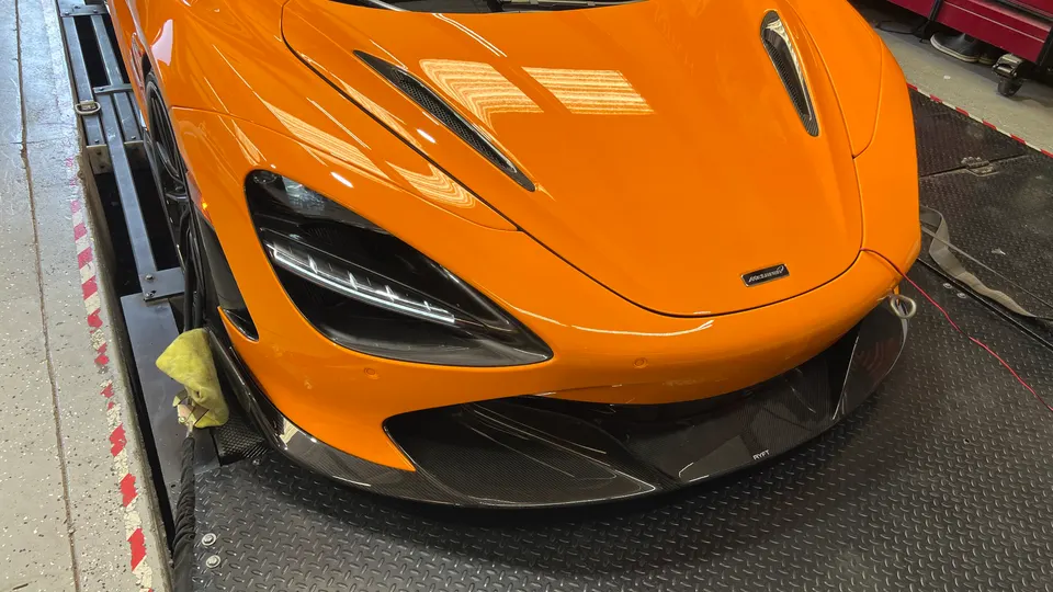 Orange McLaren supercar on a dynamometer with a carbon fiber front splitter.