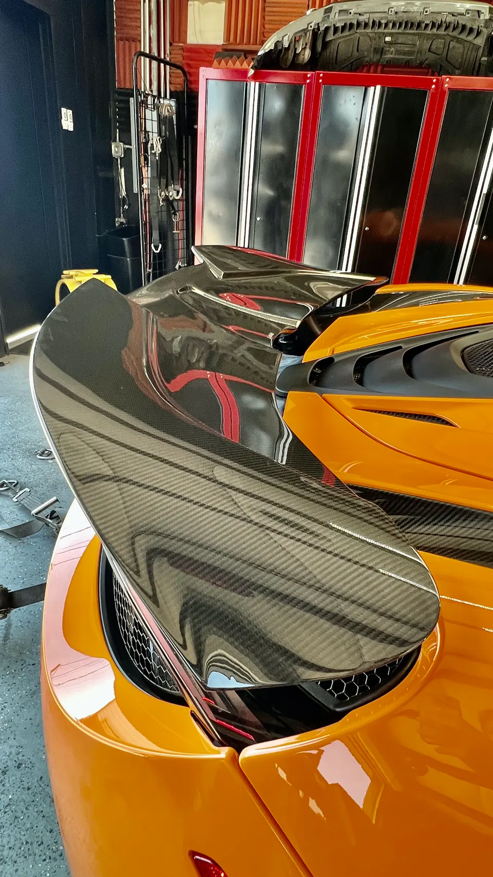 Close-up of an orange McLaren's carbon fiber rear wing in a shop setting, showcasing its intricate design.