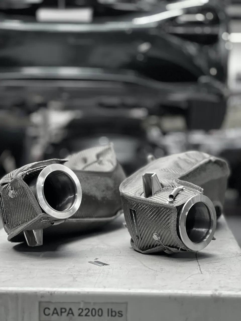 Two carbon fiber exhaust heat shields on a workbench in a performance tuning shop.