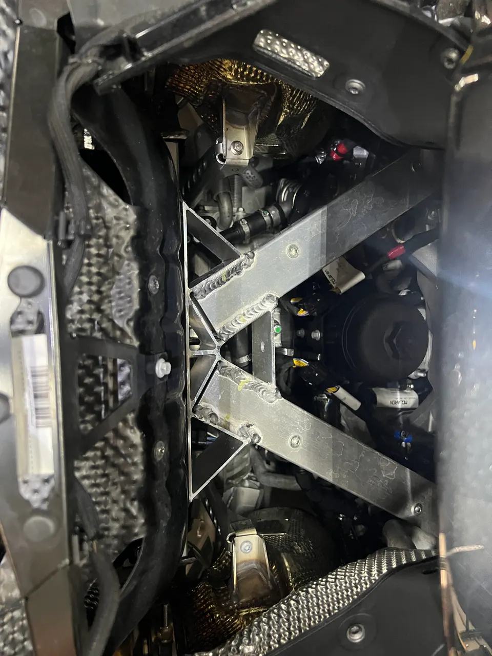 Close-up view of a McLaren engine bay showing heat shielding, oil filter, and structural bracing.
