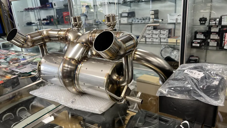 Stainless steel performance exhaust system with mufflers and tips on display in a tuning shop.