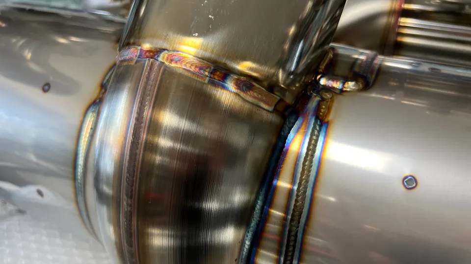Close-up detail of high-quality TIG welds on a polished stainless steel exhaust pipe, showcasing fabrication.