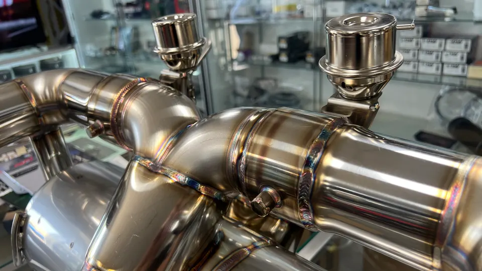 Close-up of a polished stainless steel performance exhaust system with intricate welds and wastegate actuators.