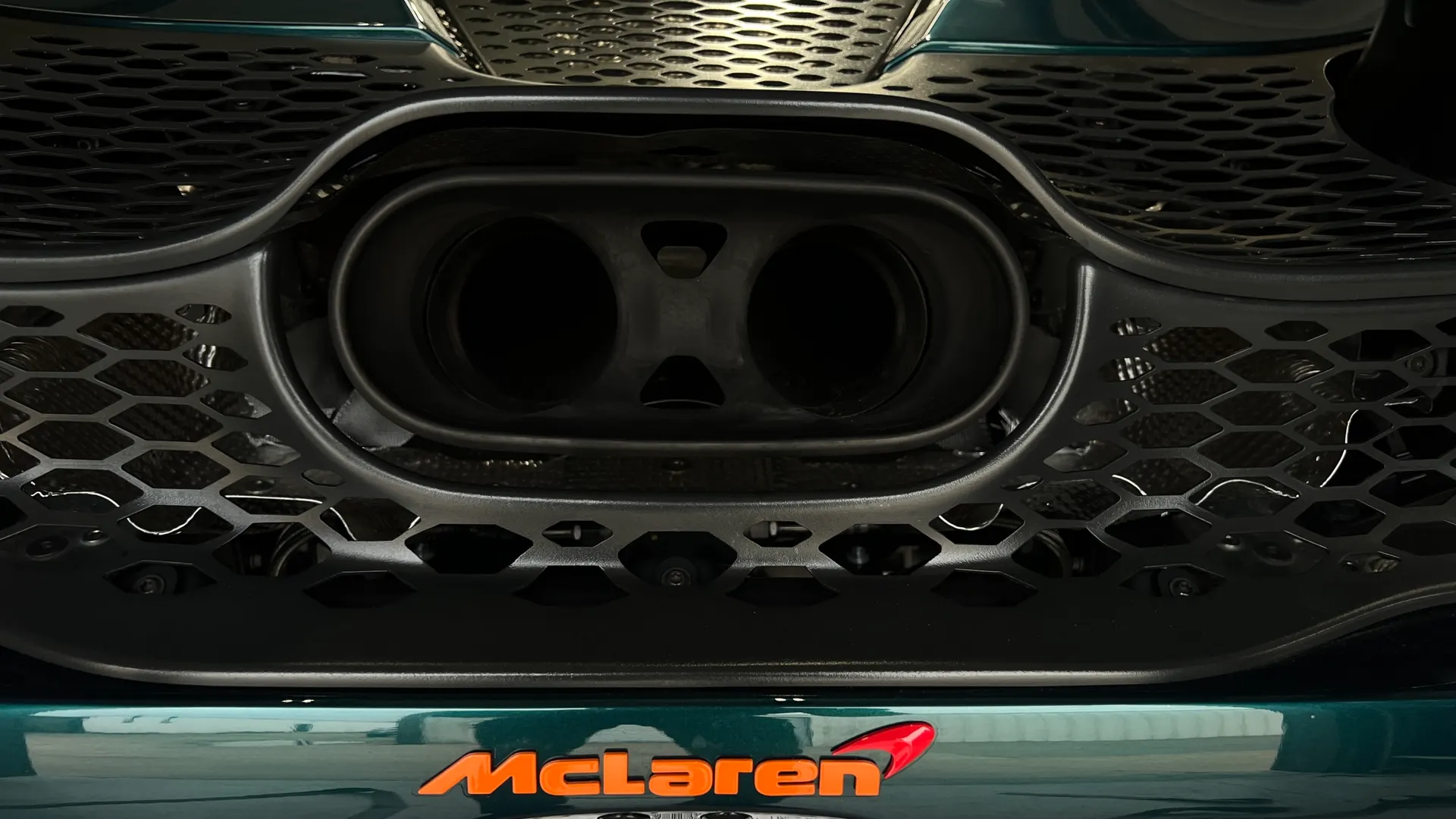 Close-up of a McLaren's dual exhaust tips and honeycomb grille, showcasing the rear design of the supercar.
