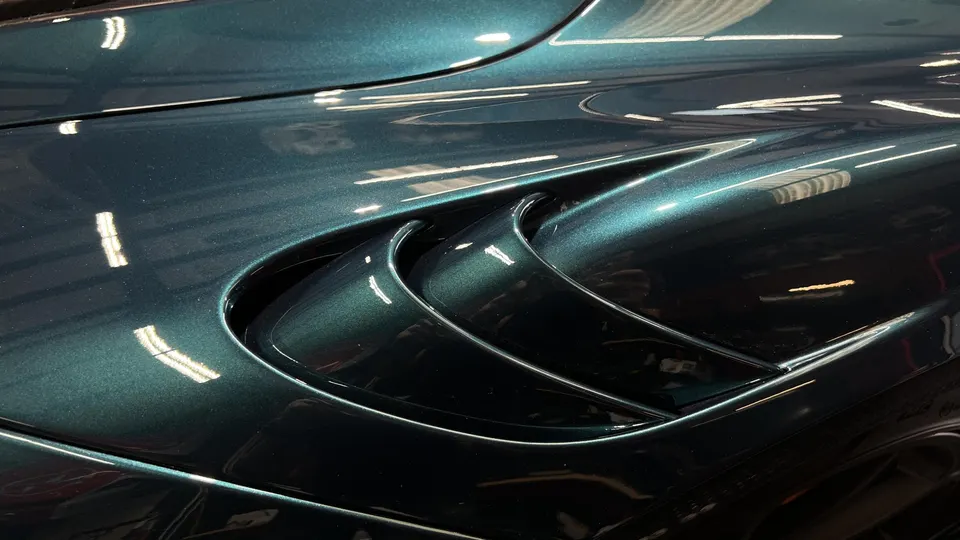 Close-up of a dark green metallic car fender with a sculpted vent, showing reflections on the paint.
