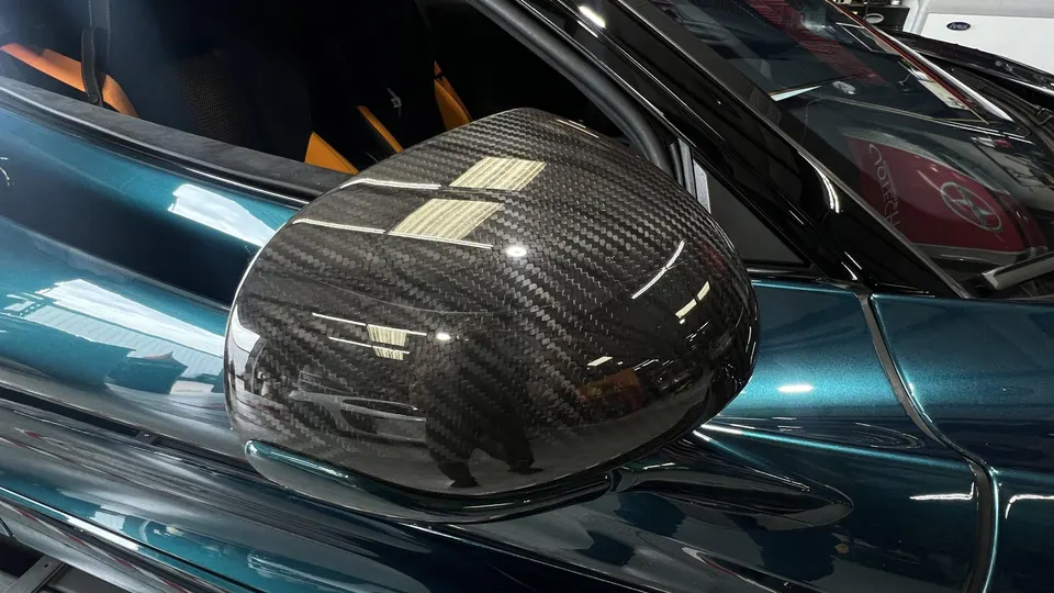 Close-up of a McLaren's carbon fiber side mirror and teal metallic paint.