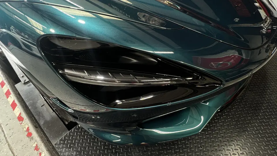 Close-up of a dark green McLaren 720S front end and headlight in a performance tuning shop.