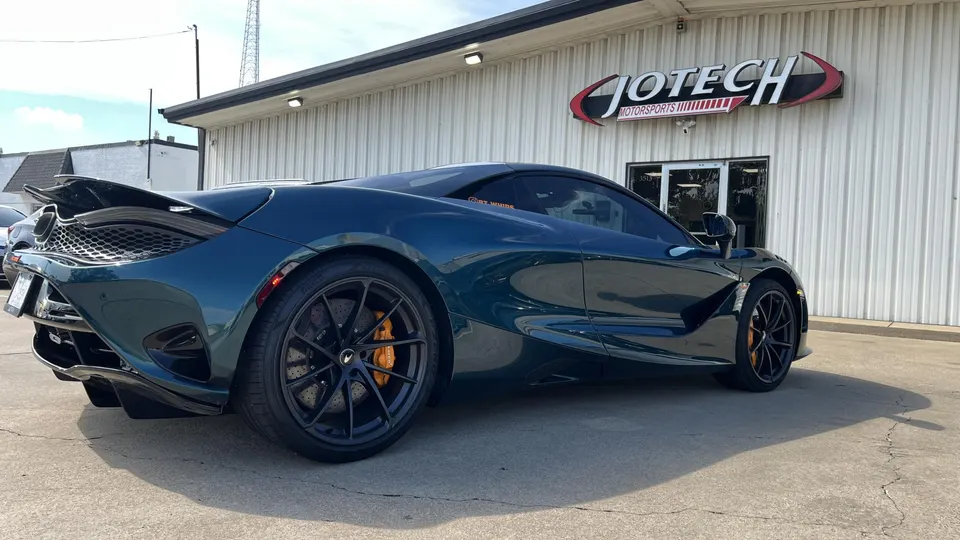 A dark green McLaren 720S parked outside the Jotech Motorsports building on a sunny day.