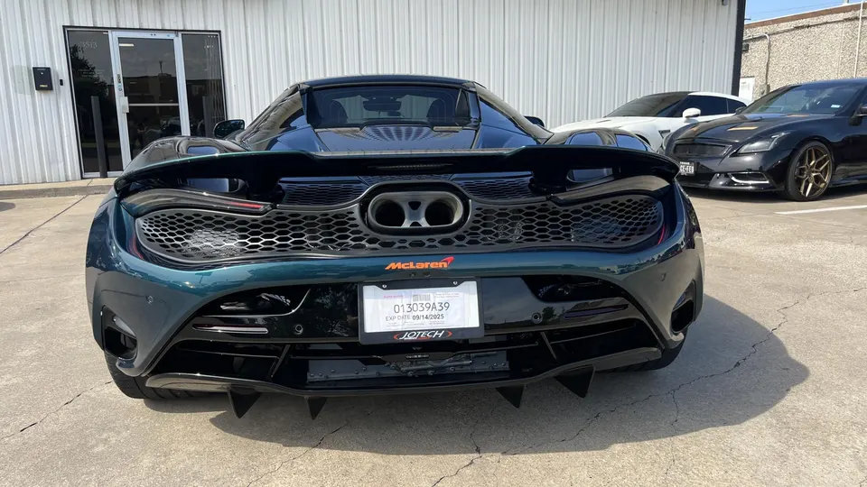 Rear view of a dark green McLaren 720S parked outside a building, highlighting its custom exhaust and rear diffuser.