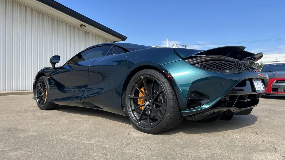 A teal McLaren 720S supercar with custom black wheels and orange brake calipers parked outside a building.