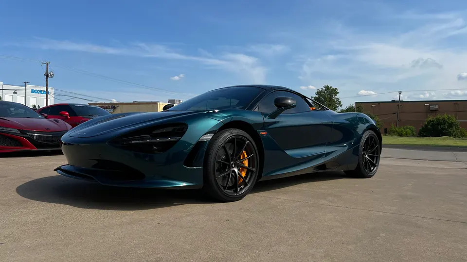 Dark green McLaren 720S supercar parked outdoors on a sunny day, with a red Acura NSX in the background.