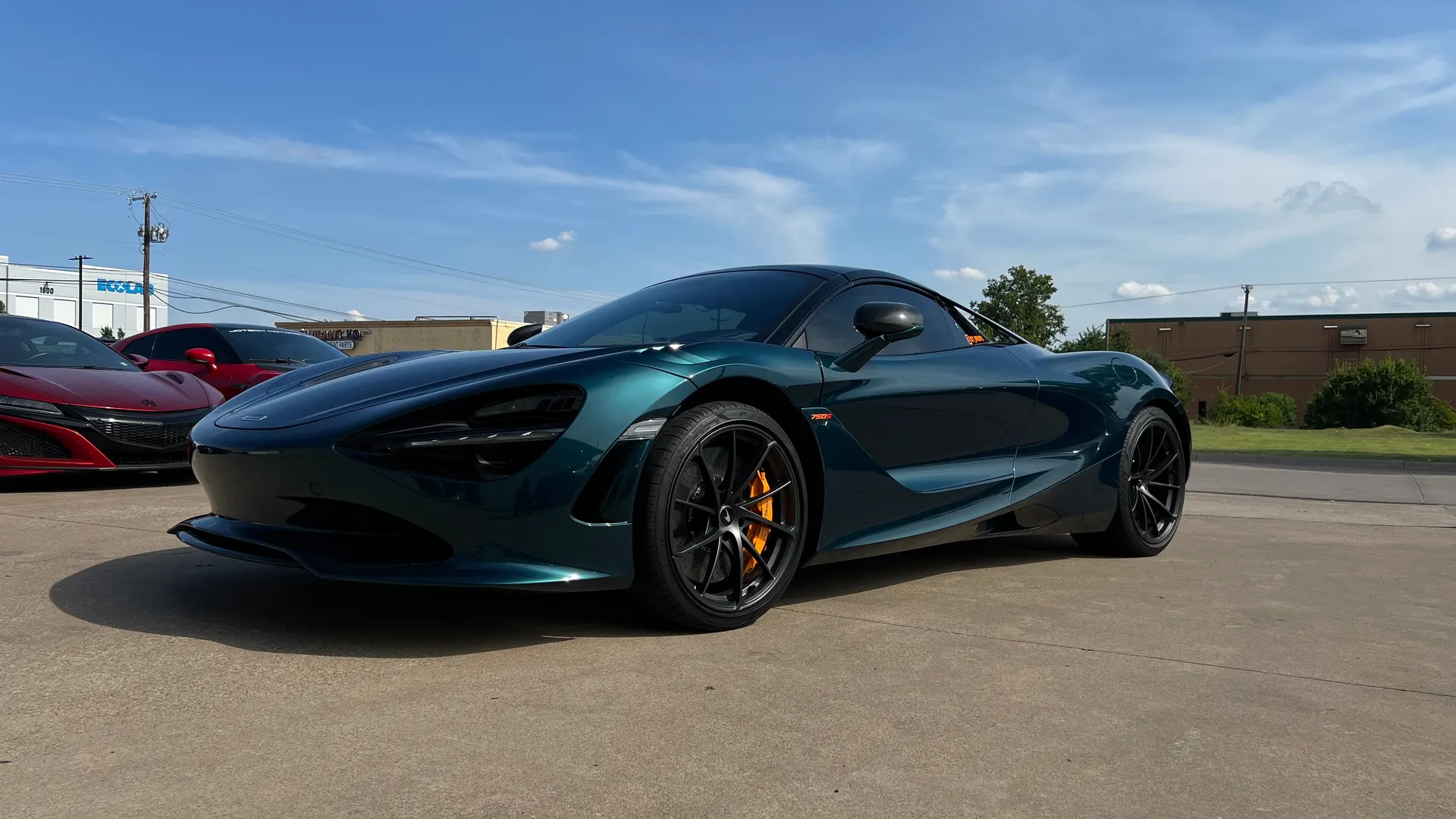 Dark green McLaren 720S supercar parked outdoors on a sunny day, with a red Acura NSX in the background.