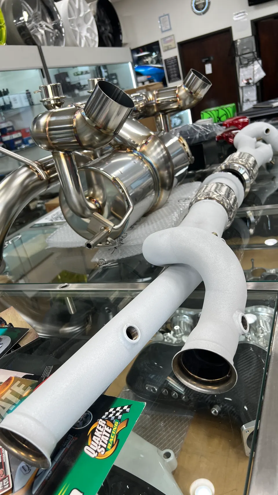 Aftermarket exhaust system components, including polished mufflers and white-coated pipes, displayed on a glass counter in a performance shop.