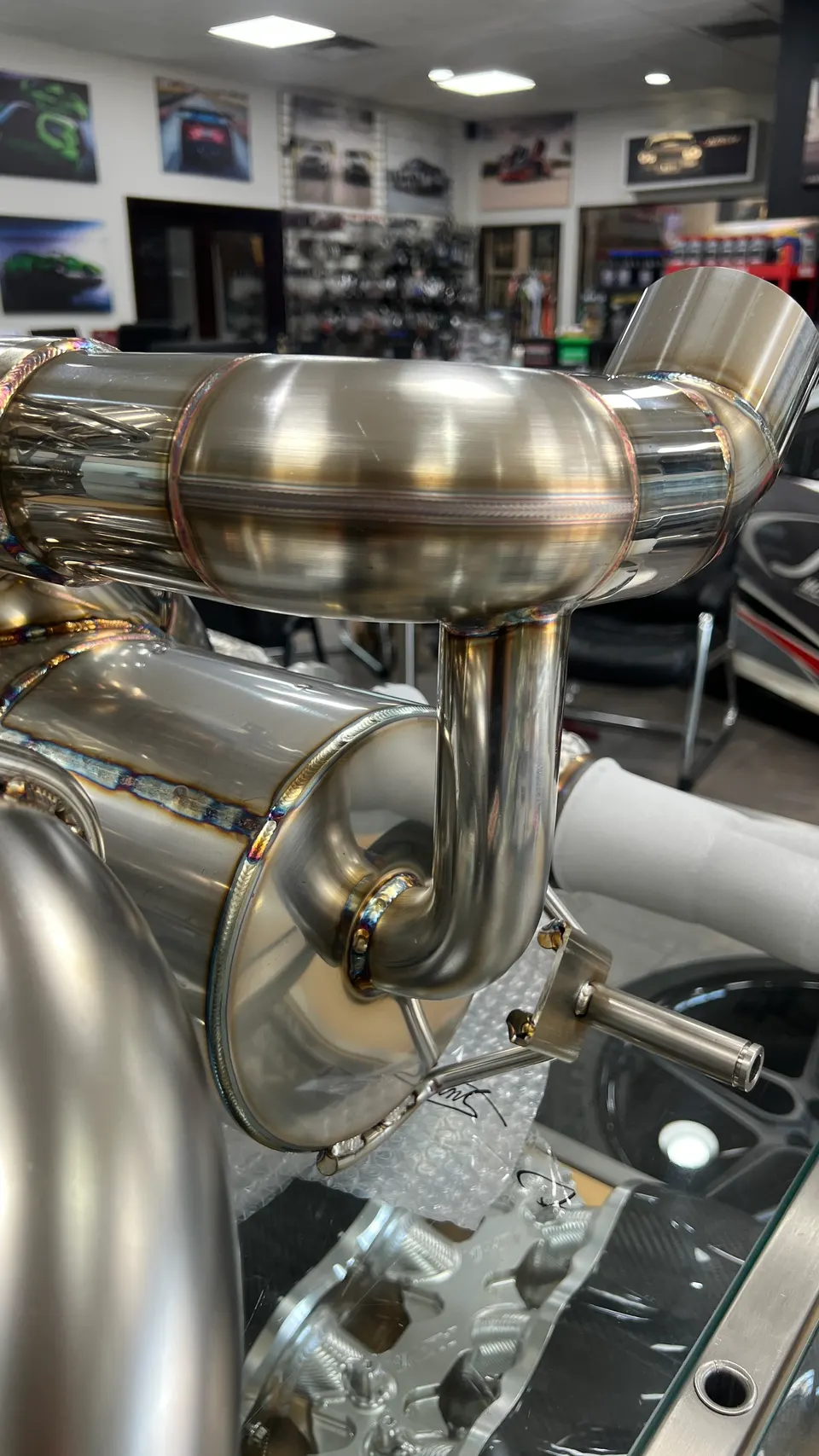 Close-up of a polished stainless steel performance exhaust system with visible welds on display in a tuning shop.