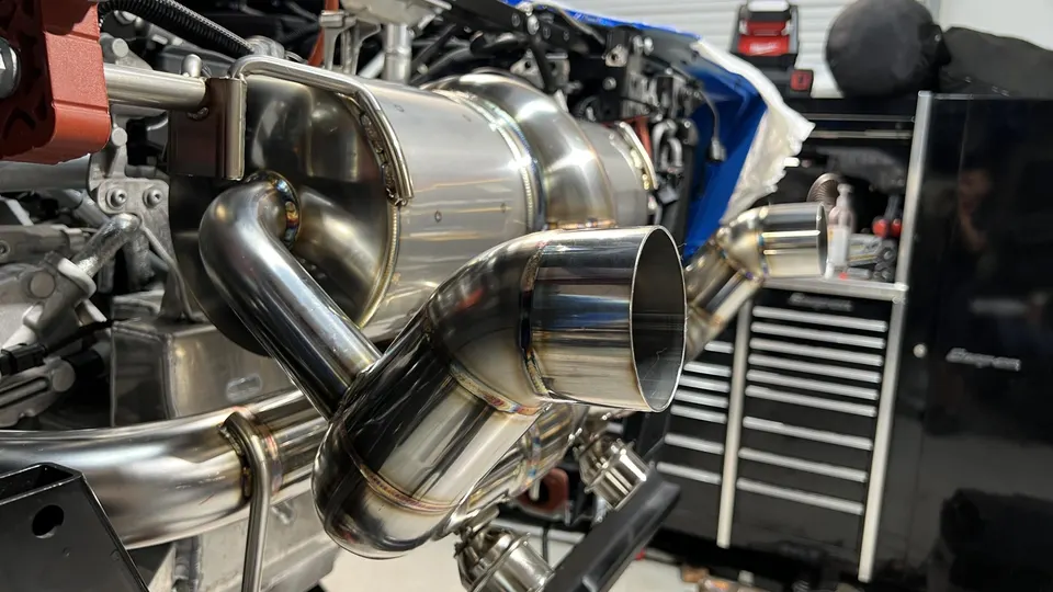 Close-up of a custom stainless steel exhaust system with visible welds being installed in a performance shop.