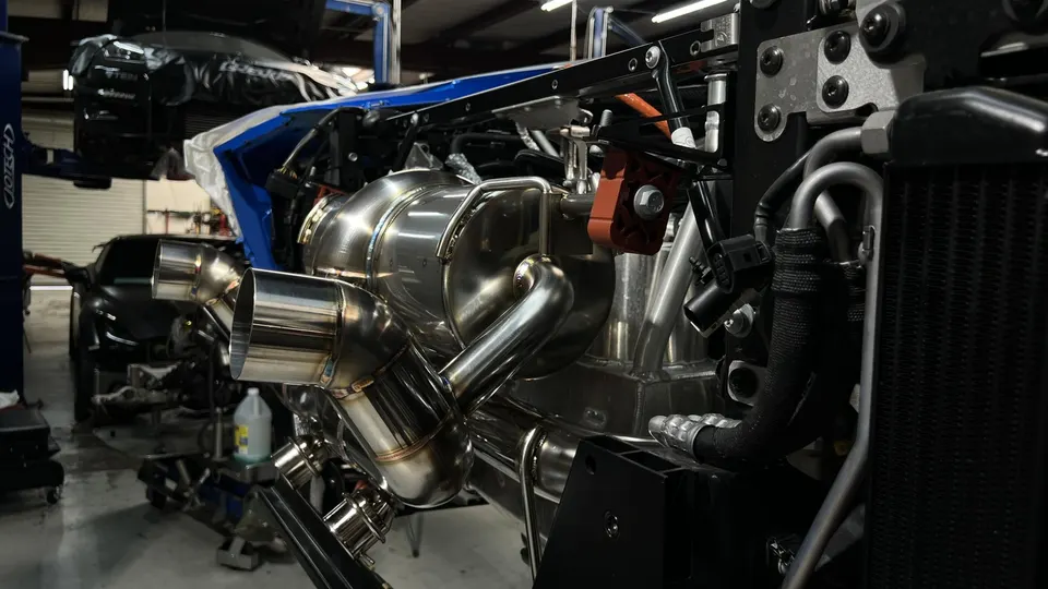 Close-up of a performance exhaust system being installed on a car in a Jotech Motorsports shop, showcasing the polished metal.