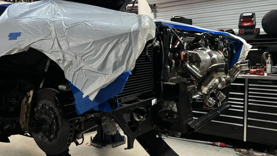 A high-performance car, possibly a Lamborghini, undergoing a custom exhaust installation in a Jotech Motorsports shop.