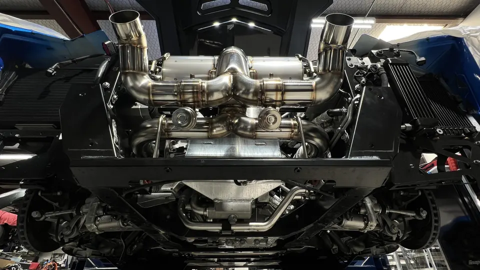 Underside view of a supercar with a custom stainless steel performance exhaust system installed in a shop.