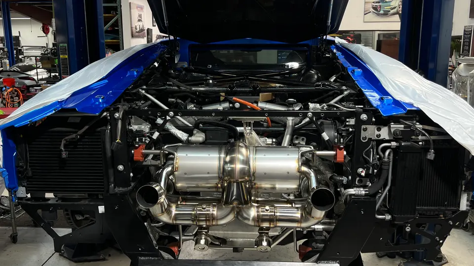 Rear view of a blue Lamborghini in a shop with its engine bay open, showcasing a new performance exhaust system installation.