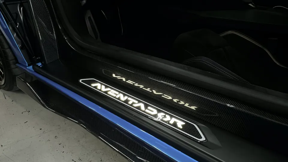 Close-up of a Lamborghini Aventador's illuminated carbon fiber door sill, showcasing the detailed interior trim.