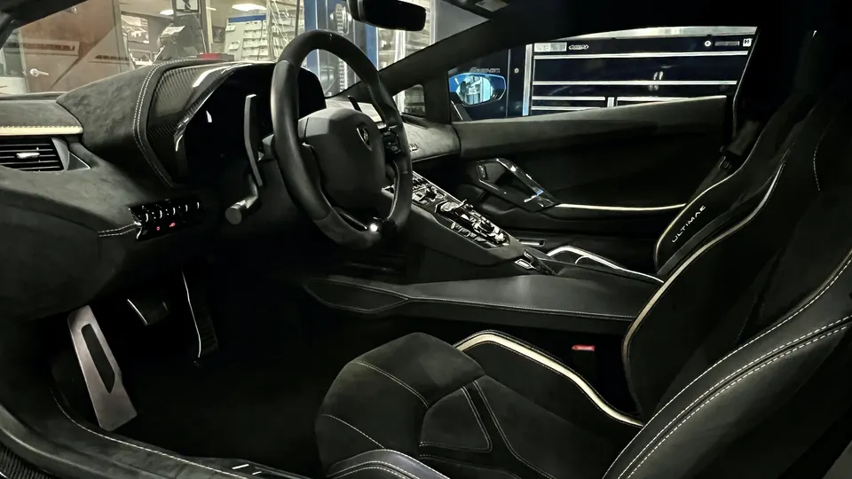 A detailed view of the black and white interior of a Lamborghini Aventador Ultimae, showing the steering wheel, dashboard, and seats.