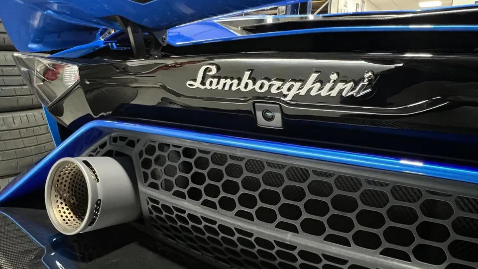 Close-up of a blue and black Lamborghini's rear, showcasing the exhaust tip, honeycomb grille, and Lamborghini badge.