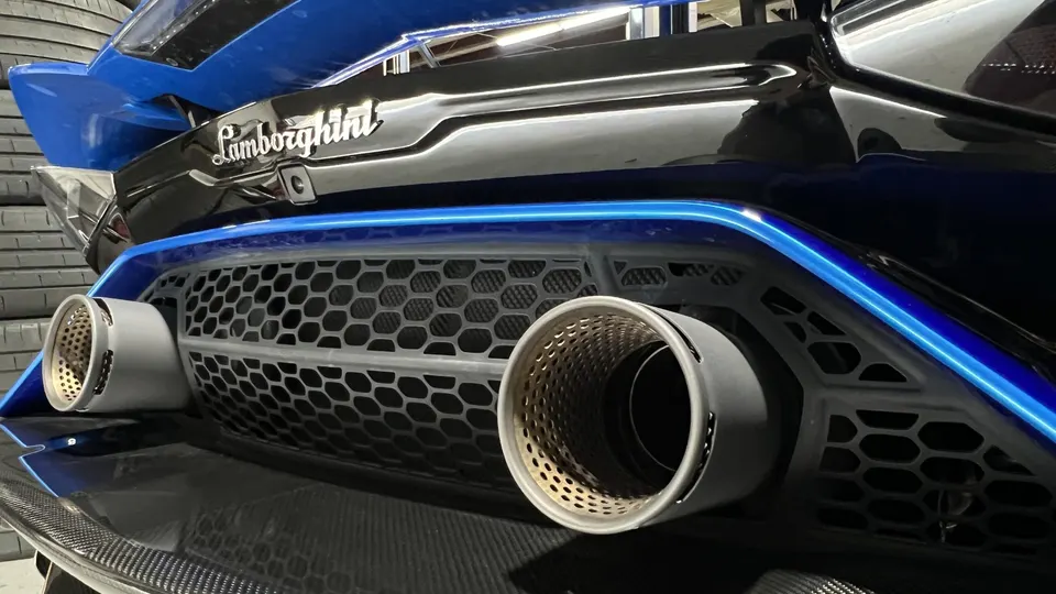 Close-up of a Lamborghini's rear showing custom exhaust tips, carbon fiber diffuser, and blue accent lighting.