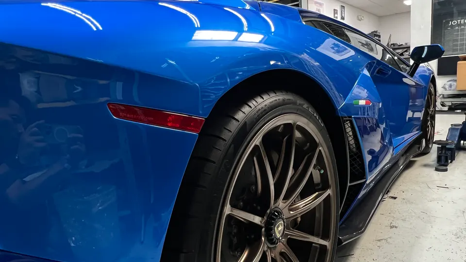 A blue Lamborghini with bronze wheels and carbon fiber side skirts in a shop.