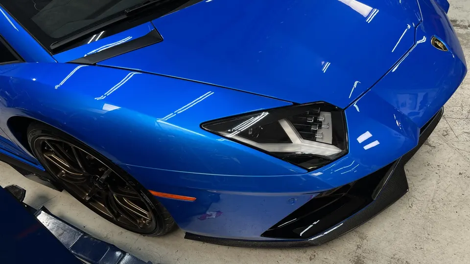Close-up of a vibrant blue Lamborghini Aventador's front end, showcasing its sleek headlight and carbon fiber splitter.